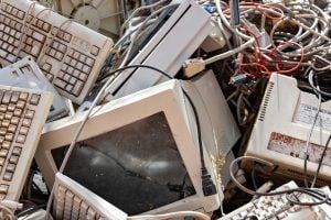 Old computer monitors, keyboards, and tangled electronic cables piled together as electronic waste (e-waste).